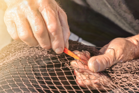 primer plano de las manos de una persona cosiendo redes de pesca