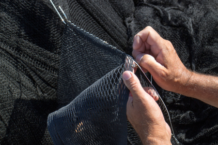 primer plano de unas manos cosiendo una red de pesca